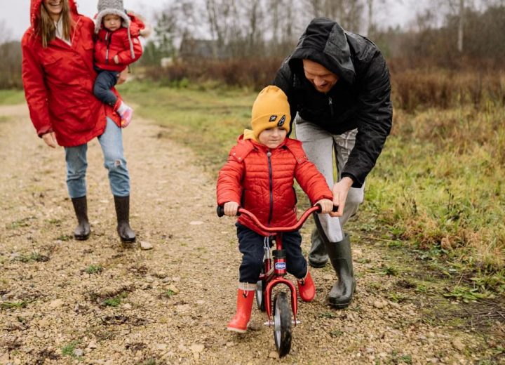 Happy family walking outdoors in fall, teaching child to ride bike.