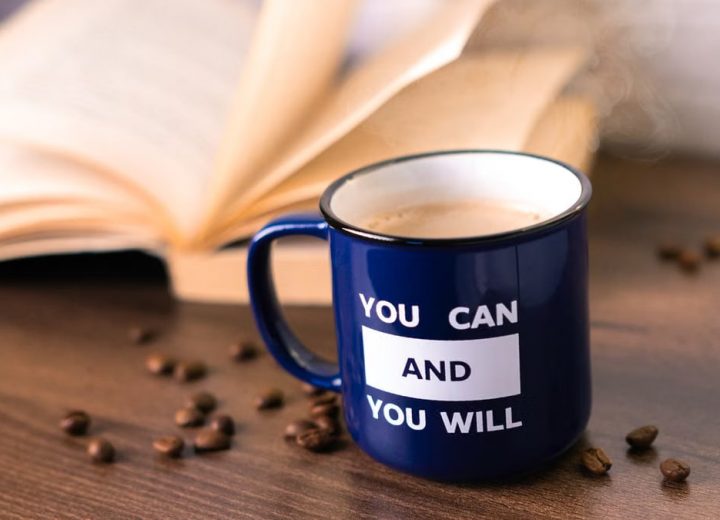 Inspirational coffee moment with a motivational quote on a mug beside an open book.